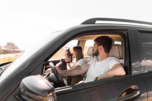 A couple sits inside a car, enjoying the moment together while a dog is playfully interacting with one of them.