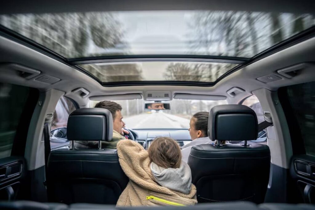 A view from the backseat of a car, showcasing a child nestled in a blanket, with two adults seated in front, cruising on a tree-lined road.