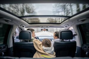 A view from the backseat of a car, showcasing a child nestled in a blanket, with two adults seated in front, cruising on a tree-lined road.