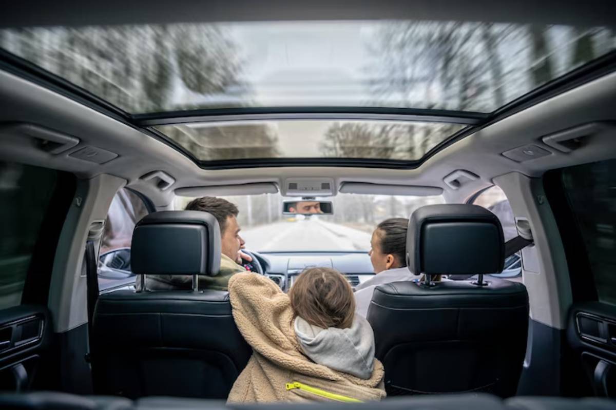 A view from the backseat of a car, showcasing a child nestled in a blanket, with two adults seated in front, cruising on a tree-lined road.