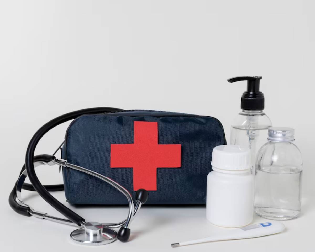 A blue medical kit with a red cross, stethoscope, thermometer, and various medication bottles arranged on a light background.