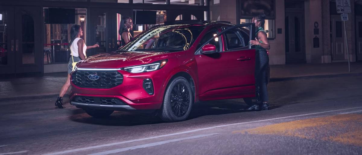 A sleek red Ford SUV parked on a city street at night, with two stylish women interacting near the open door.