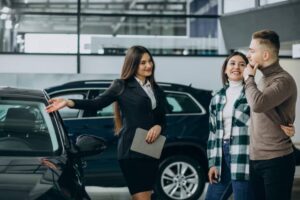 A car saleswoman gestures towards a vehicle, while a couple, dressed casually, listens attentively in a modern showroom.