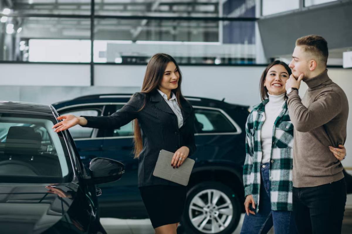 A car saleswoman gestures towards a vehicle, while a couple, dressed casually, listens attentively in a modern showroom.