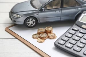 A model car next to stacks of coins and a calculator on a clipboard, symbolizing car financing or budgeting concepts.