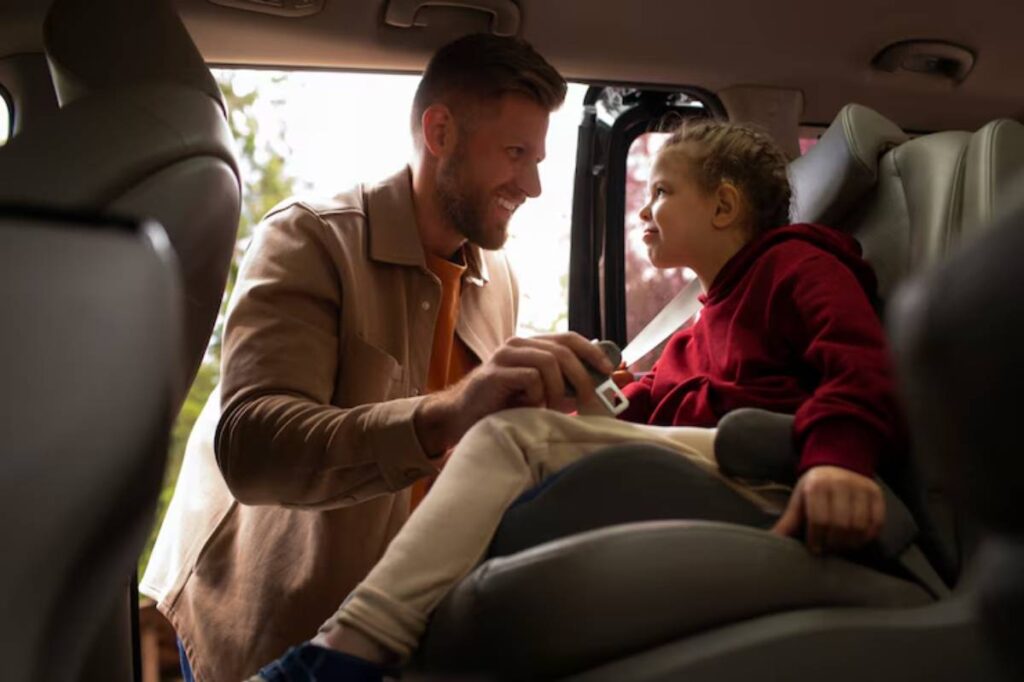 A man secures a child in a car seat, focused and attentive, with sunlight streaming through the open door.