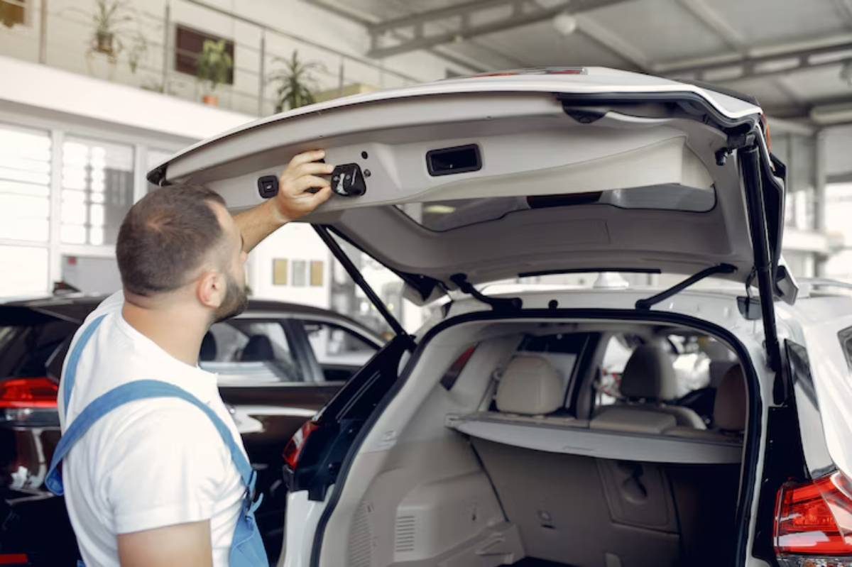 A mechanic adjusts the control panel inside the trunk of a white SUV in a car dealership's service area.