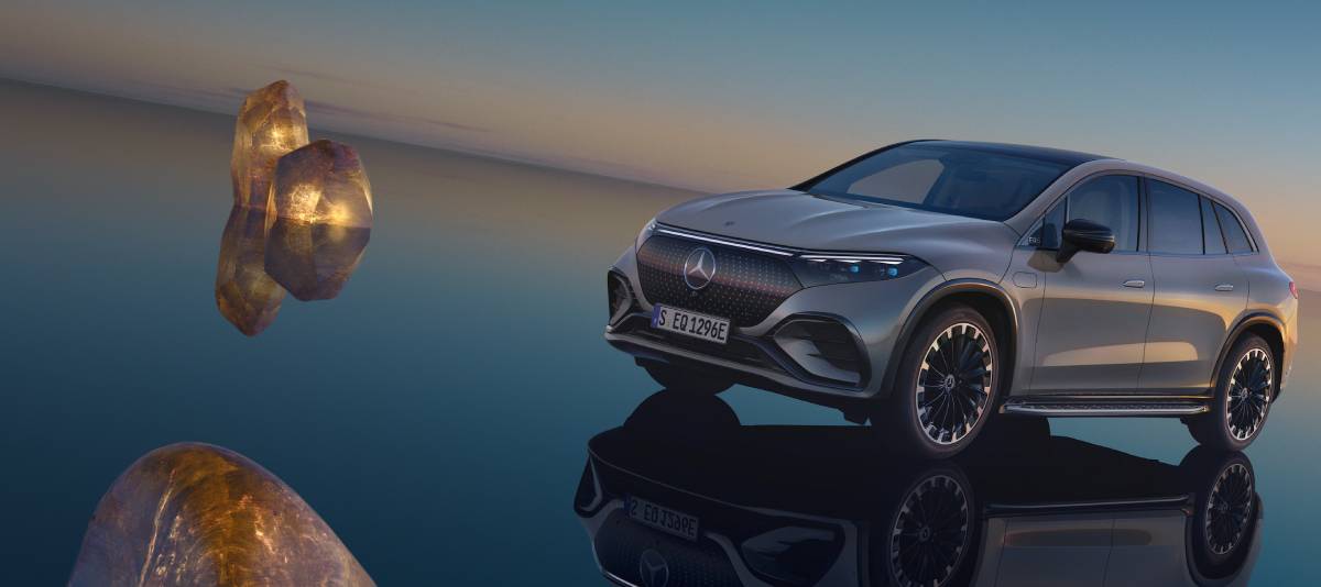 A sleek silver Mercedes EQS SUV parked on a reflective surface with glowing rocks, set against a serene twilight sky.