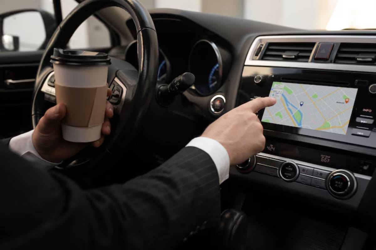A businessman in a suit navigates using a touchscreen map while holding a coffee cup, seated in a car.
