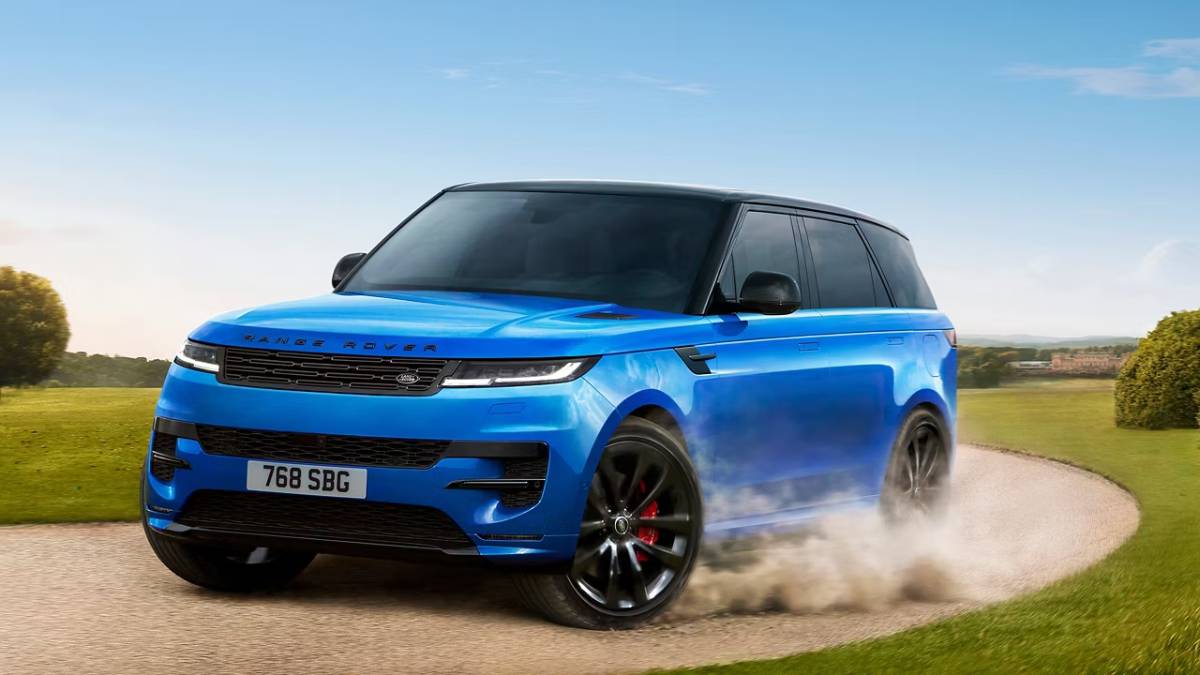 A blue Range Rover Sport accelerates on a winding dirt road, kicking up dust against a clear sky and vibrant green landscape.
