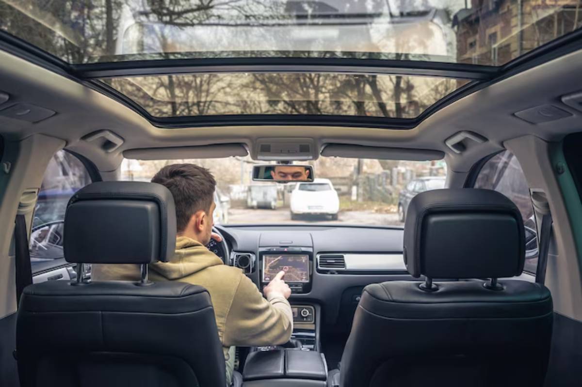 A driver seated in a modern car with a panoramic sunroof, using a touchscreen navigation system while looking ahead.