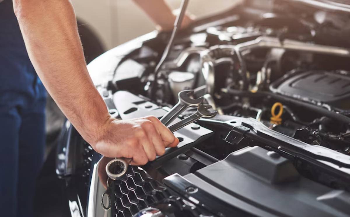 A mechanic's hand grips a wrench while working on a car's engine, showcasing automotive maintenance in a workshop setting.