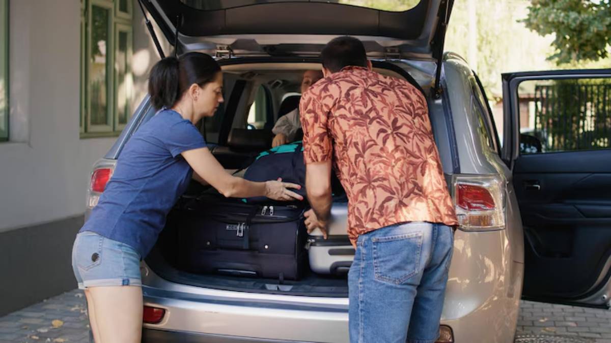 Two individuals are loading luggage into the back of a silver SUV while a third person sits inside the vehicle.