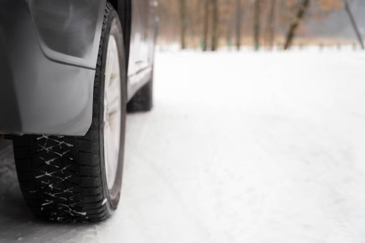 Close-up of a car's winter tire on a snowy road, showcasing its tread designed for enhanced grip in cold conditions.