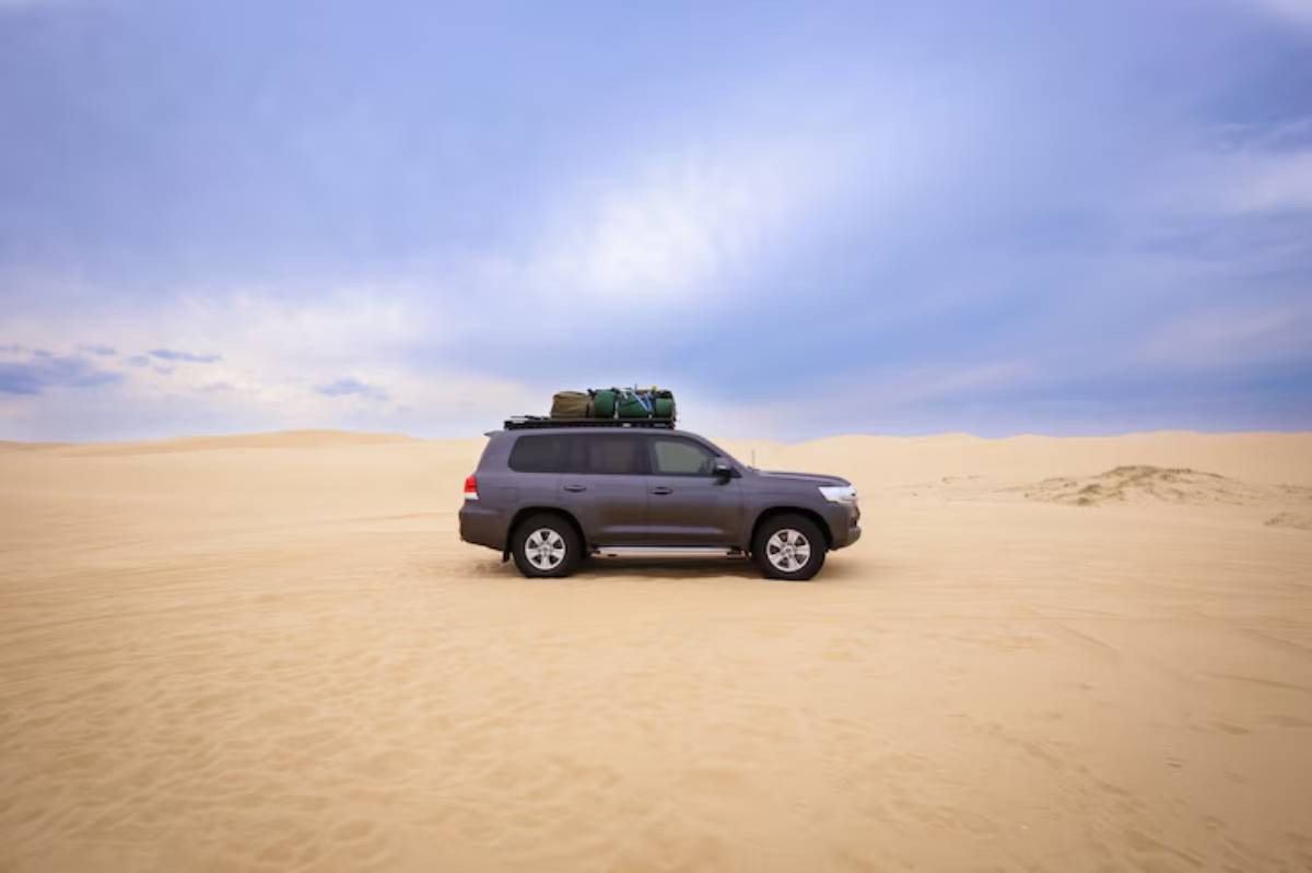 An SUV parked on a vast sandy desert with a blue sky and soft clouds, showcasing an adventurous outdoor scene.