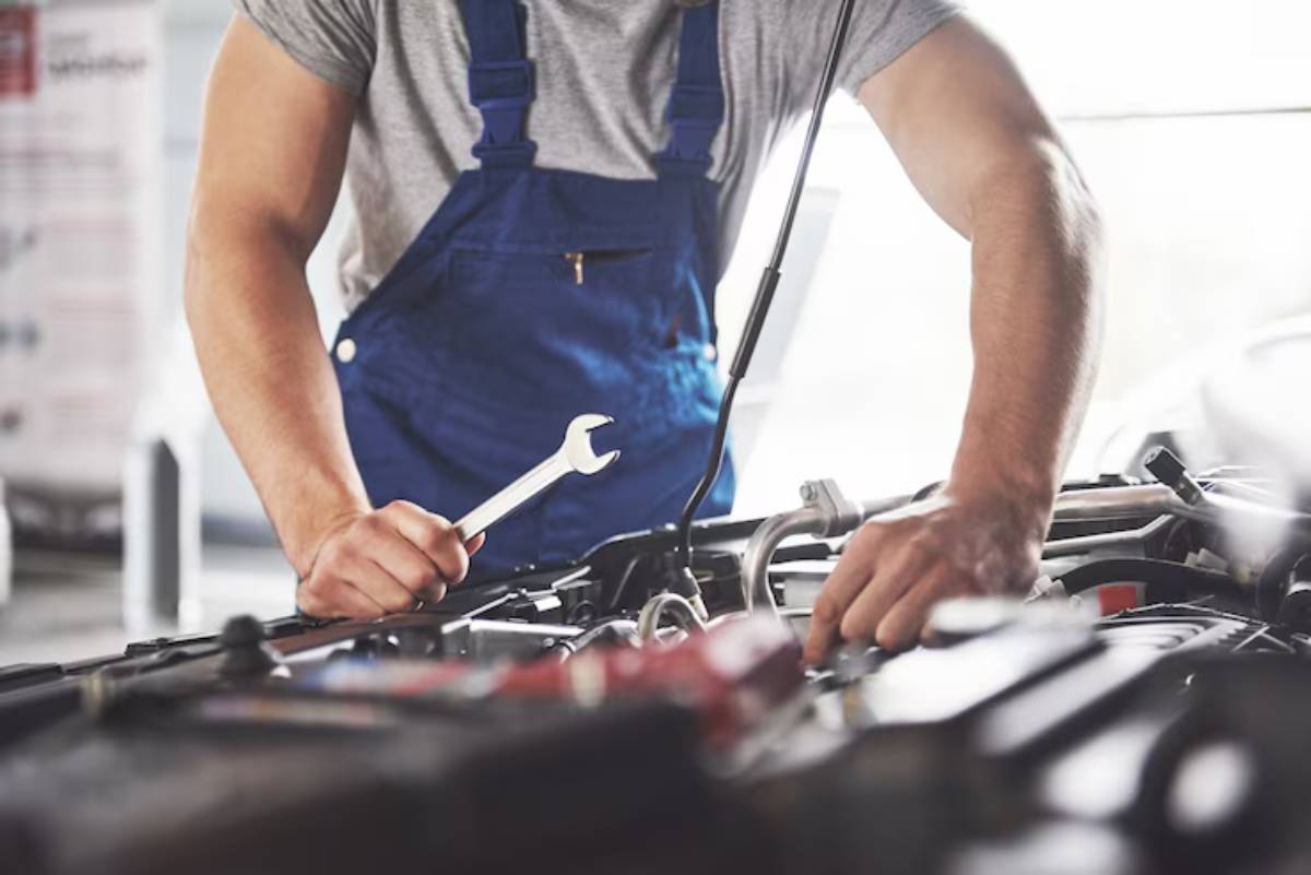 A mechanic in blue overalls works on an engine, using a wrench to troubleshoot or perform repairs in a bright garage.